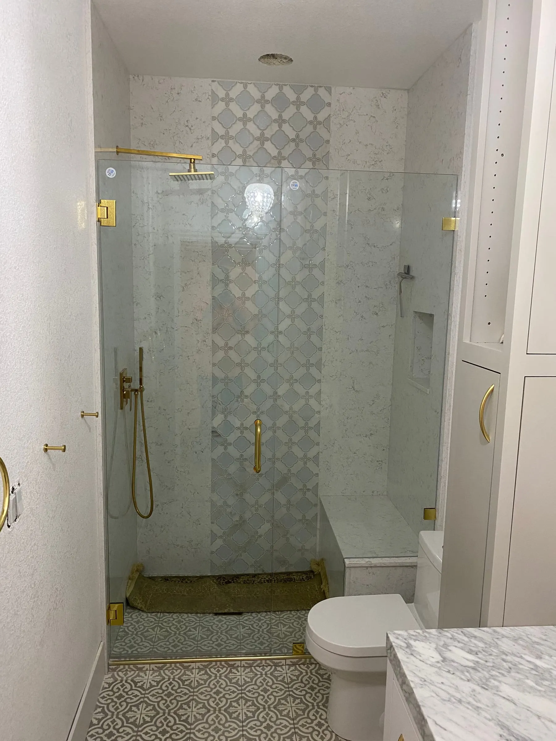 Frameless shower door with brushed gold hardware and patterned tile